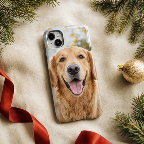 Capa de telemóvel com a foto de um golden retriever, entre ramos de pinheiro e fita vermelha